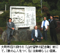 写真：大町市旧八坂村の「山村留学の記念碑」前にて。「農の心人をつくる」は素晴らしい言葉。