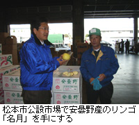 写真：松本市公設市場で安曇野産のリンゴ「名月」を手にする